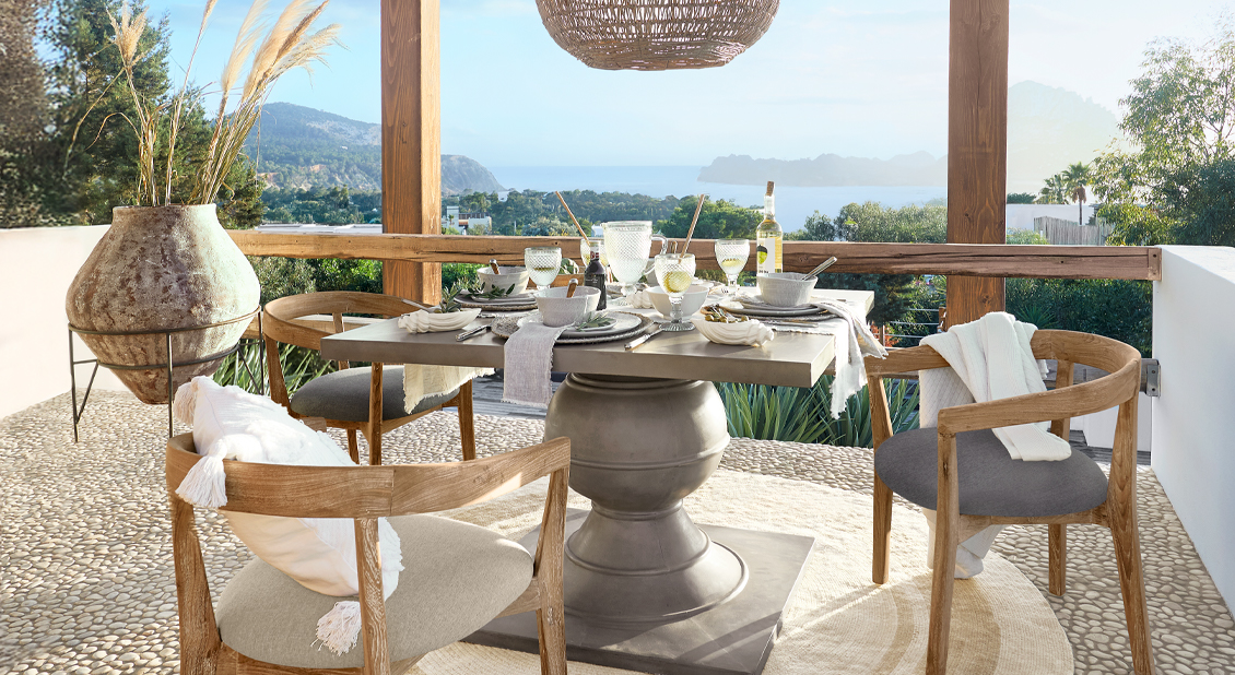 Esstisch mit Betonplatte und Holzstühlen auf Terrasse mit Meerblick und Dekorationen