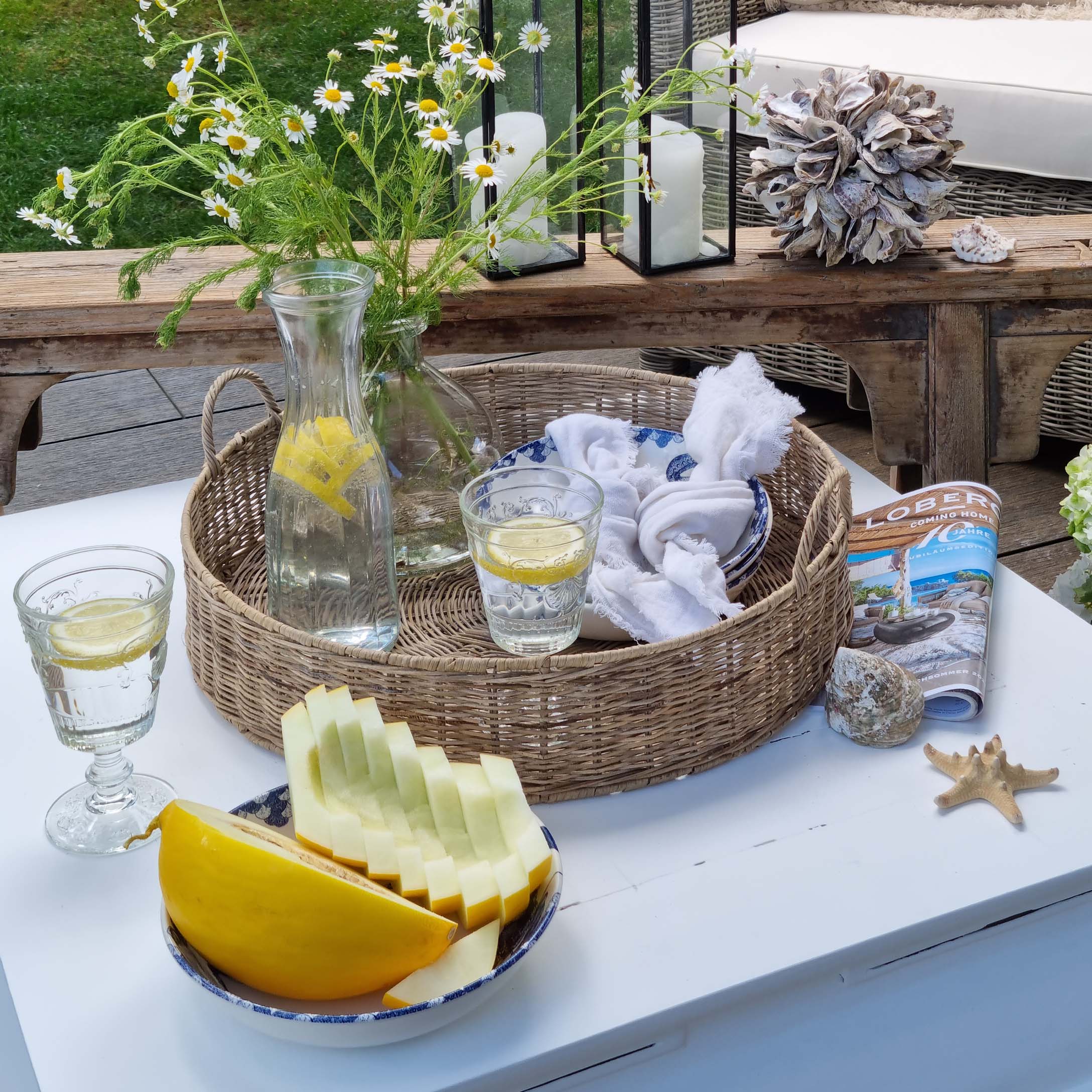 Runder Korb aus Rattan mit Zitronenwasser und Glas auf weissem Gartentisch dekoriert