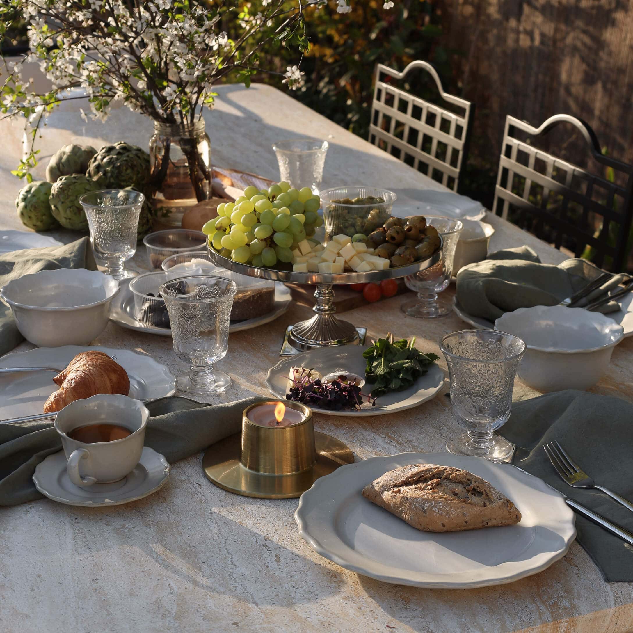 Steintisch mit weissem Geschirr, Kerze und Tablett mit Trauben, Käse und Oliven im Freien