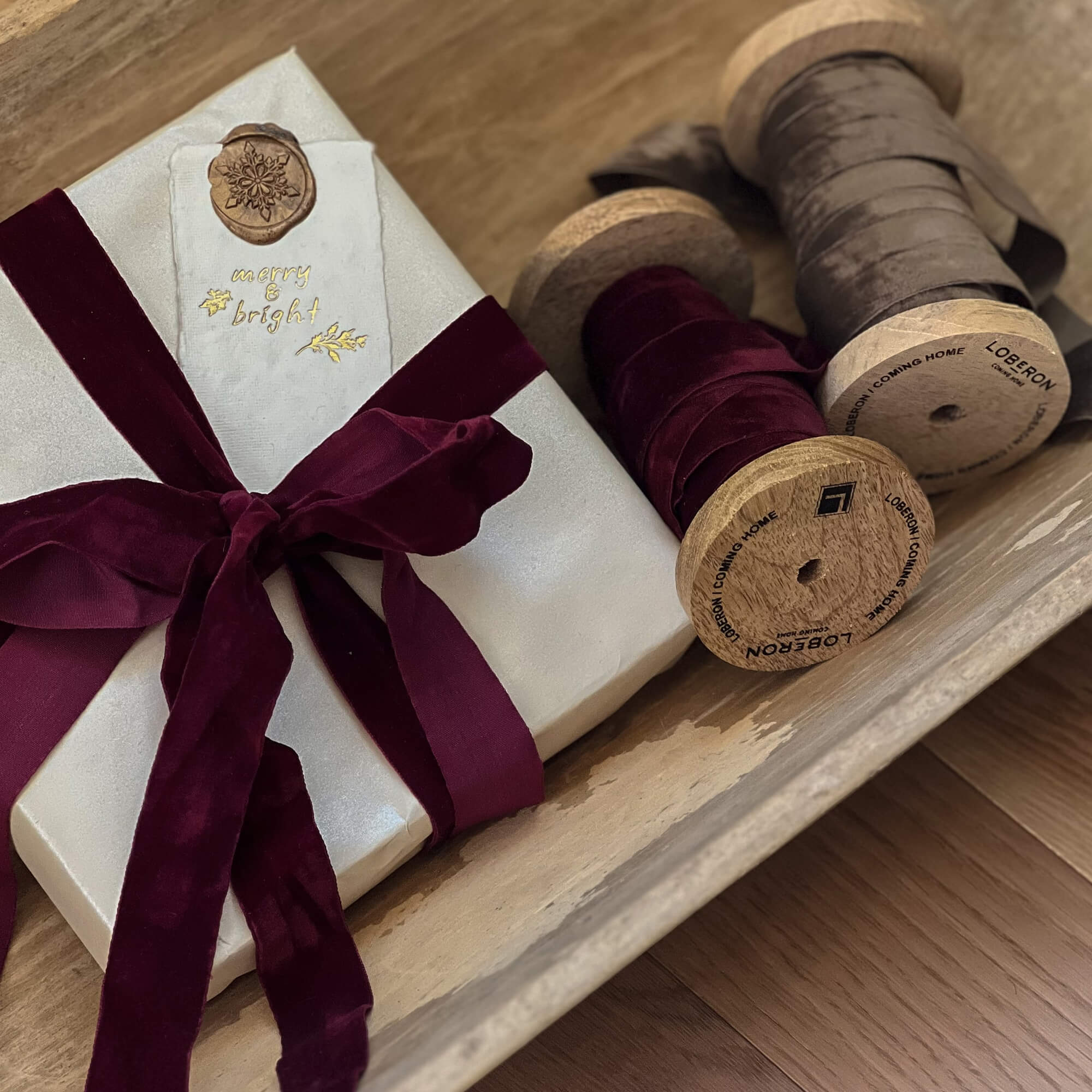 Geschenk in weissem Papier mit bordeauxrotem Samtband und mit Bändern dekorierten Holzspulen