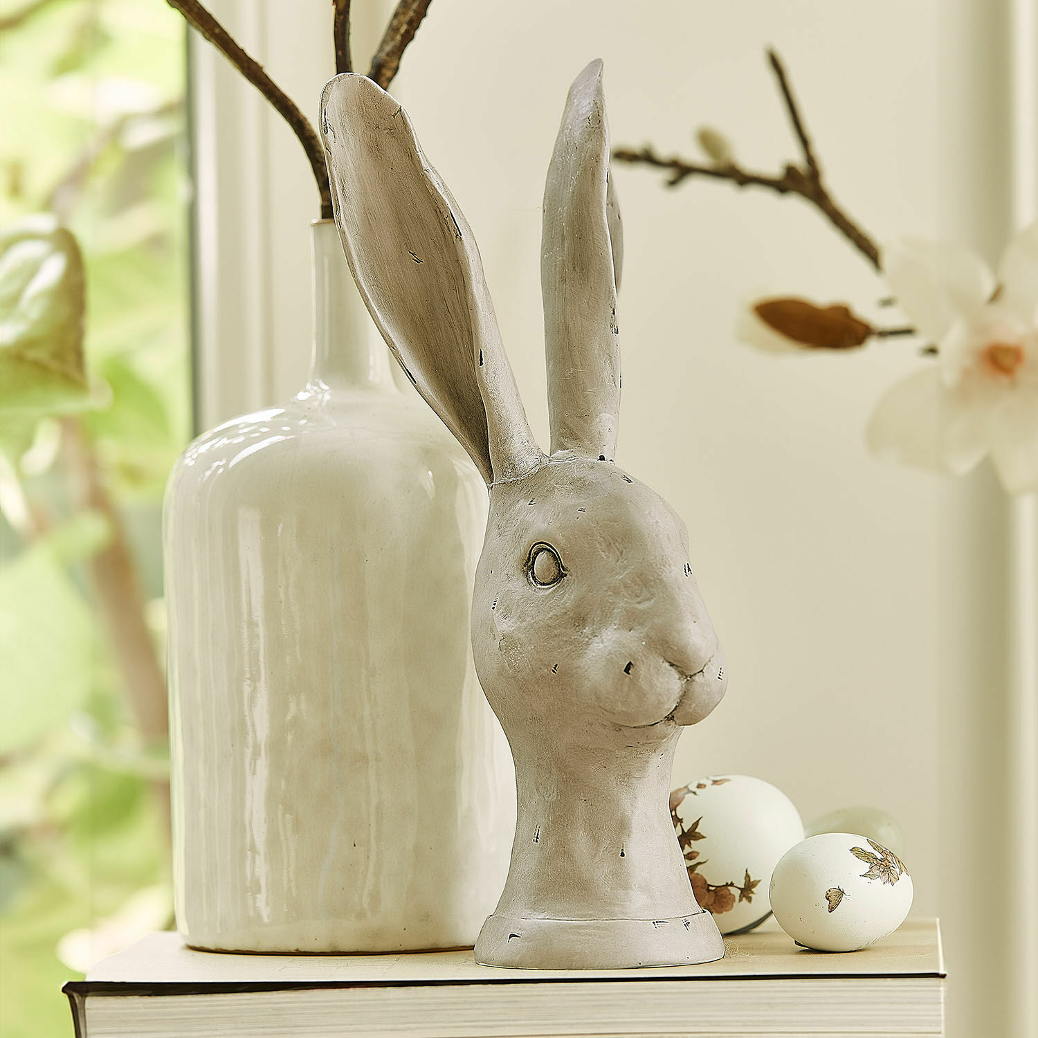 Hase Najirah Dekorative Hasenfigur aus grauer Keramik auf Buch mit verzierten Ostereiern