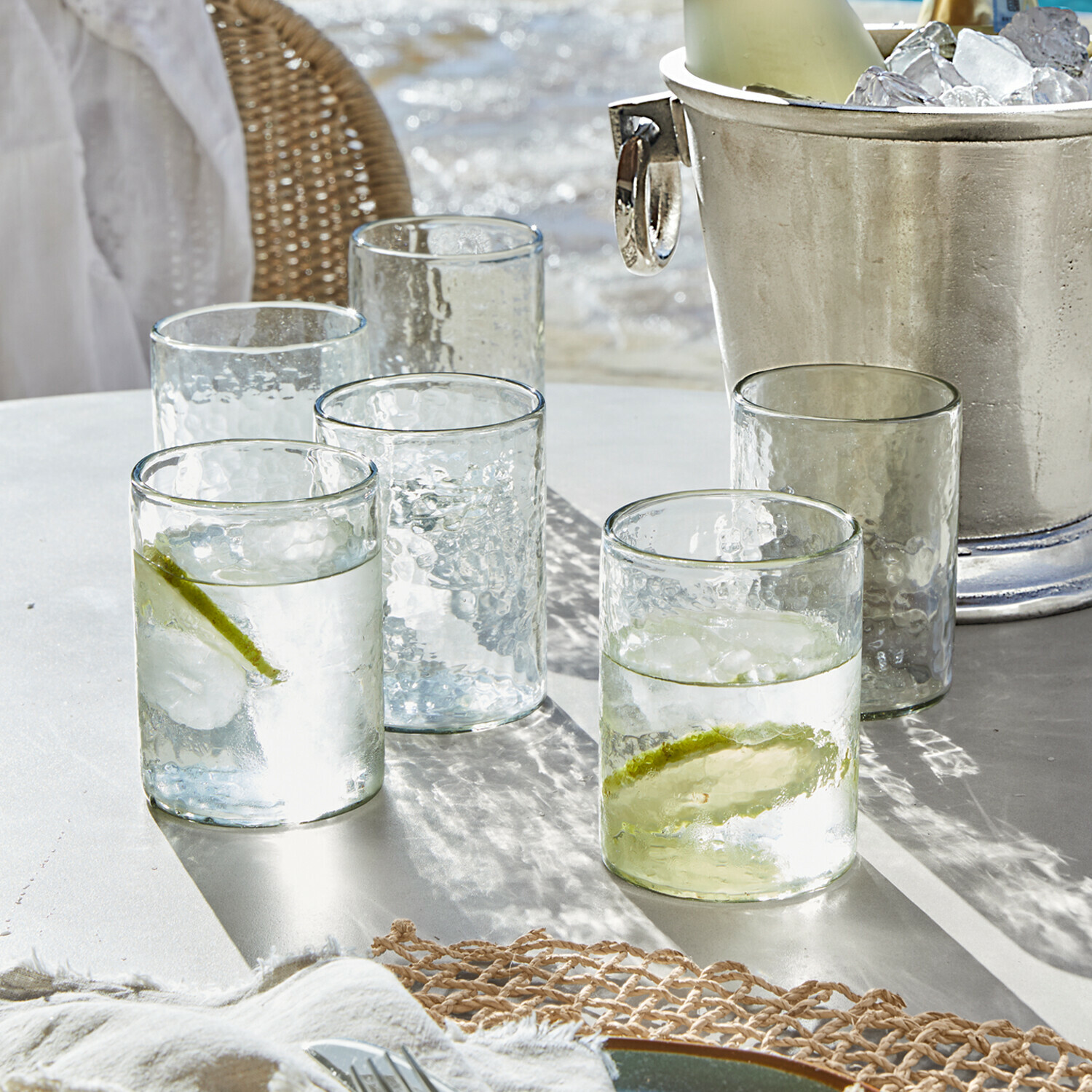 Gläser aus klarem, strukturiertem Glas mit Limettenscheiben und Eiswürfeln auf weissem Tisch