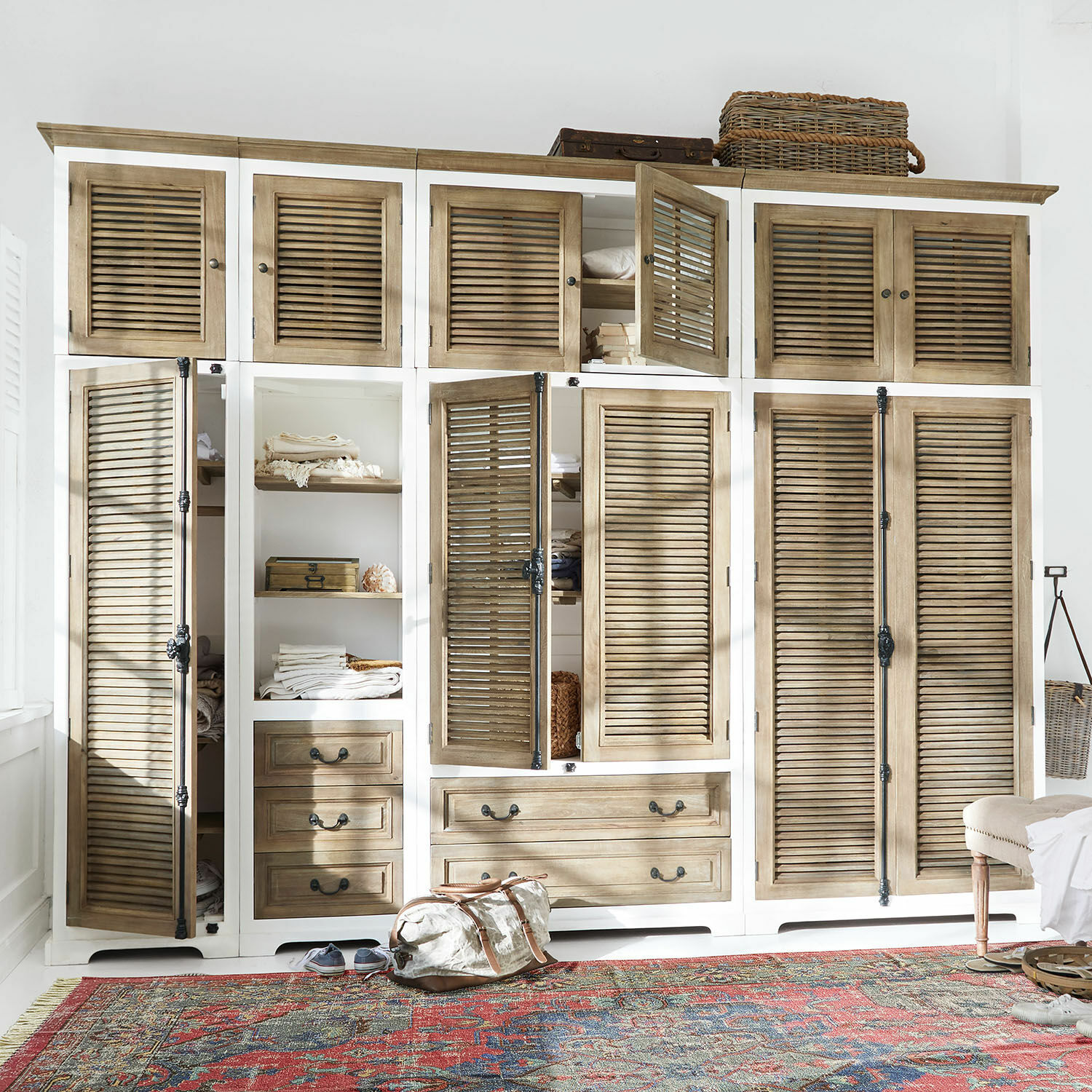 Schrank-Set Daviau Grosser Holzschrank in Weiss und Natur mit Lamellentüren und Schubladen auf buntem Teppich.