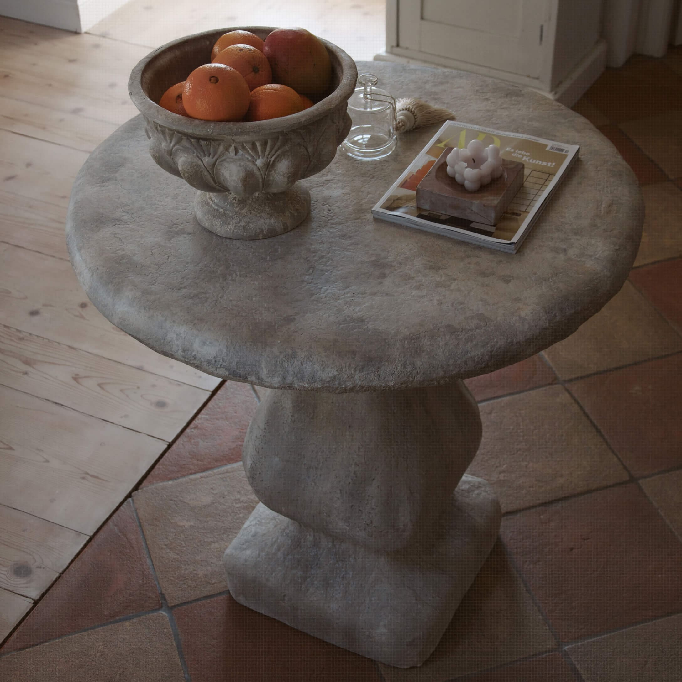 Runder grauer Steintisch mit Obstschale und dekorativen Gegenständen auf der Oberfläche