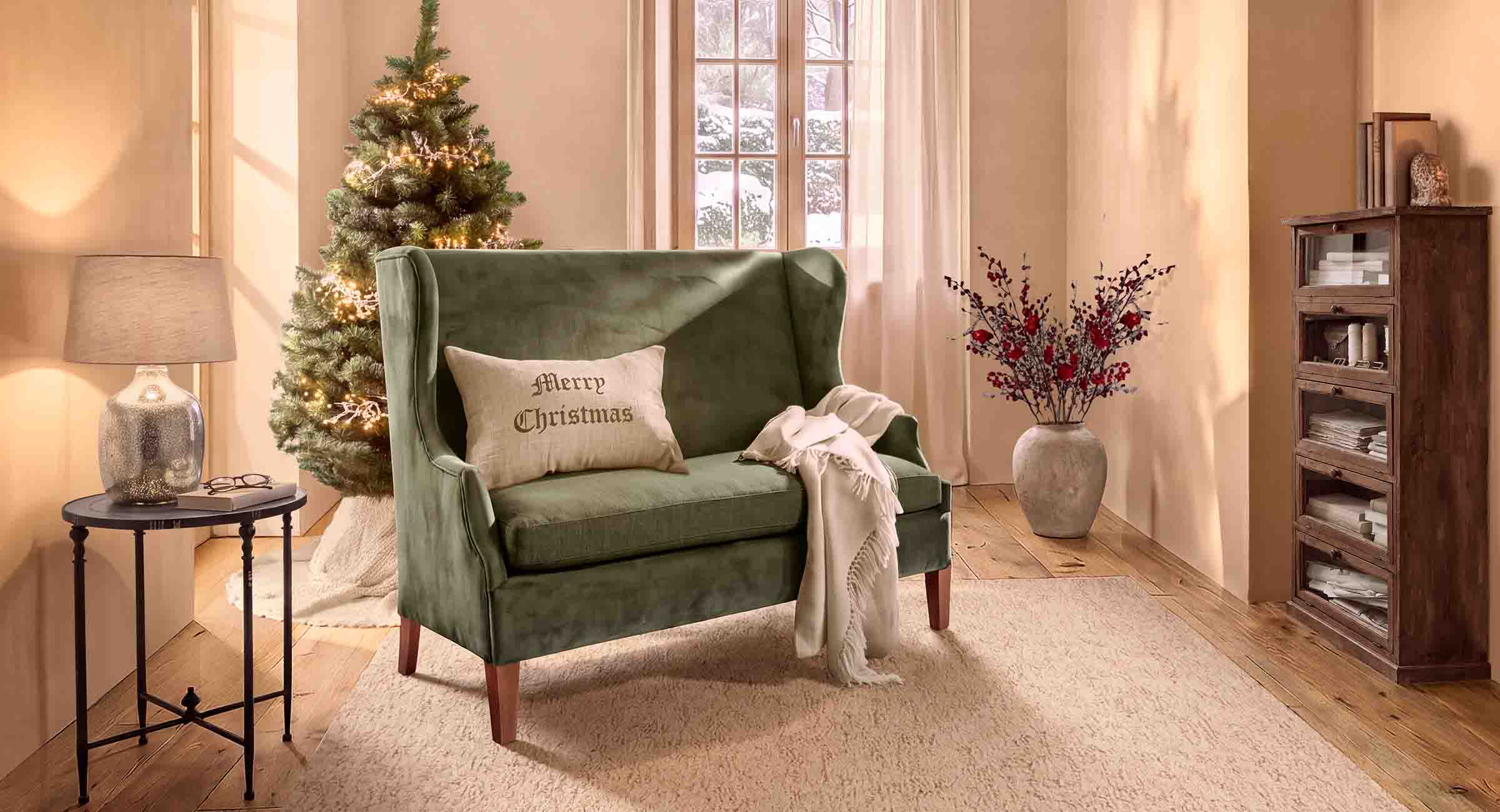 Grünes Samtsofa mit Merry Christmas Kissen in gemütlichem Wohnzimmer mit Weihnachtsbaum