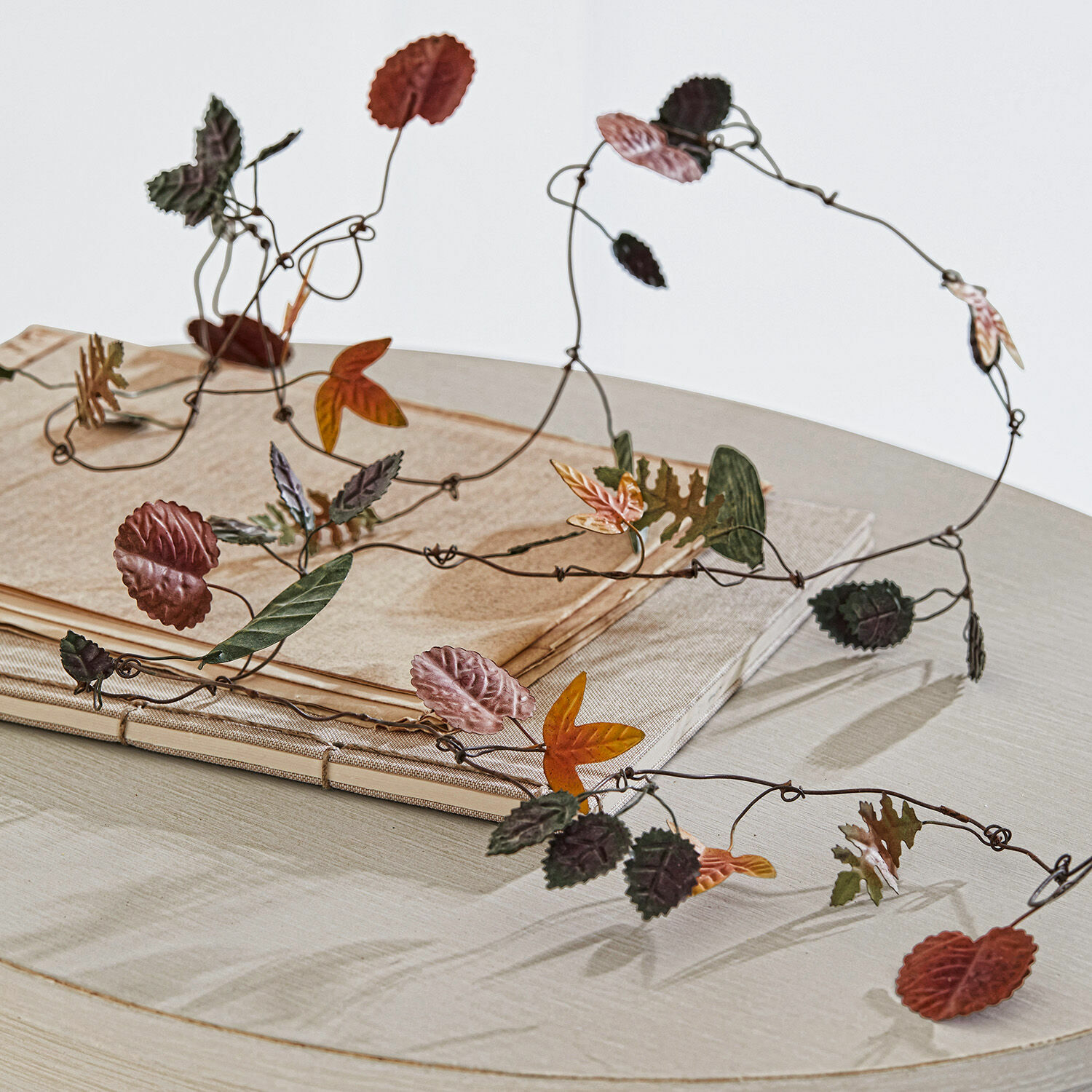 Dekorative Metallgirlande mit bunten Herbstblättern auf hellem Tisch