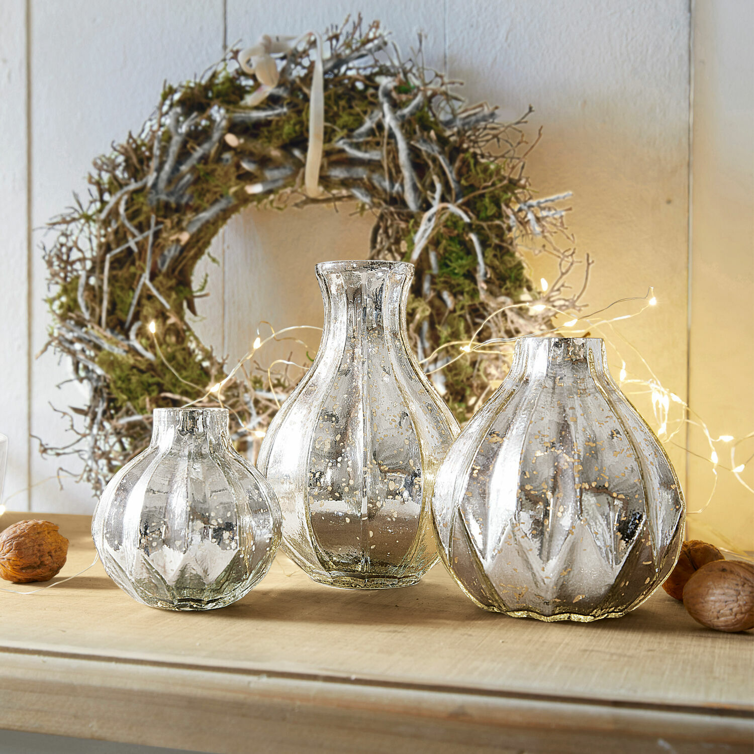 Vase 3er Set Frido Drei dekorative silberne Glasvasen auf einem Holztisch vor einem natürlichen Kranz mit Lichterkette
