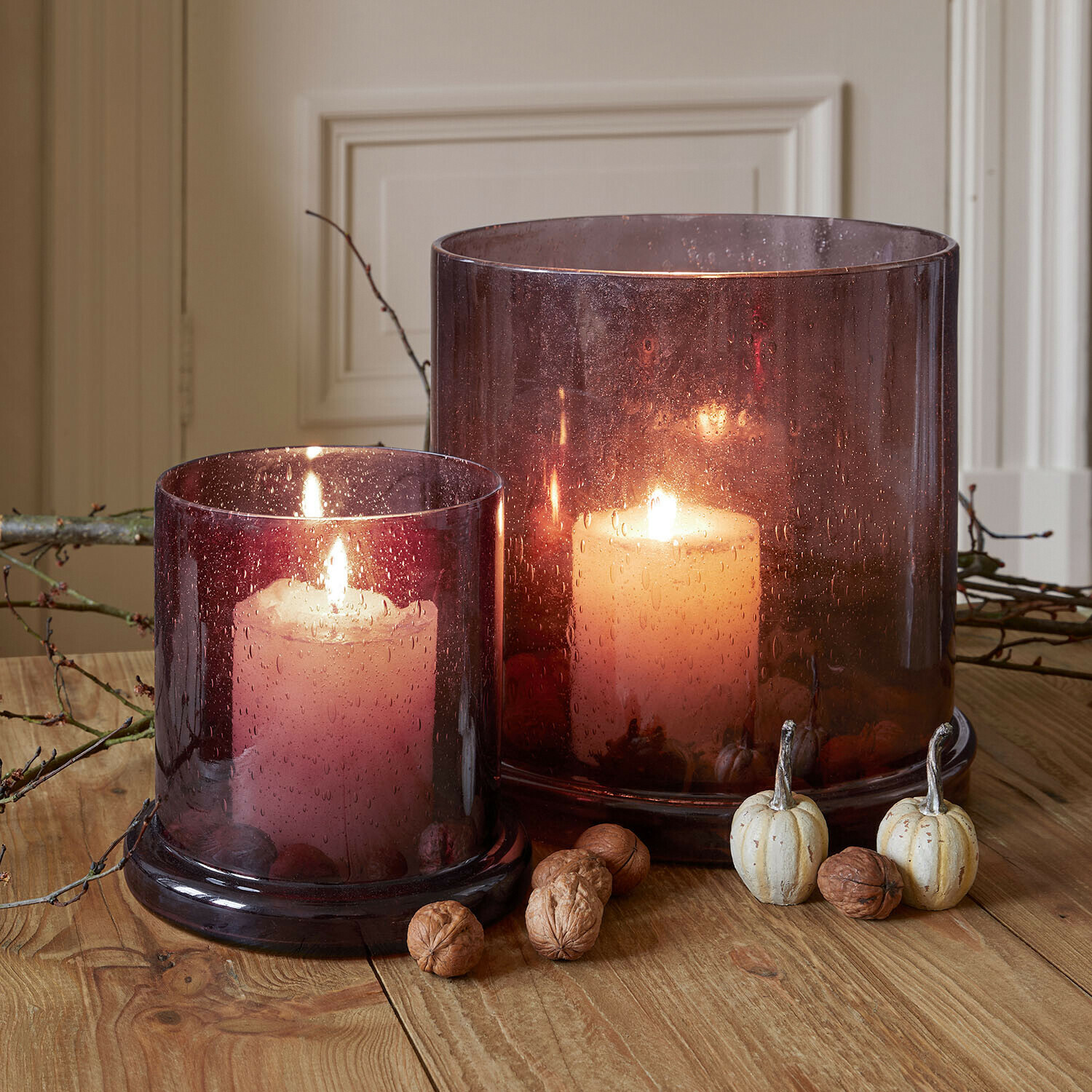 Windlicht 2er Set Saffrone Zwei brennende Kerzen in violetten Glaswindlichtern auf Holztisch mit herbstlicher Dekoration