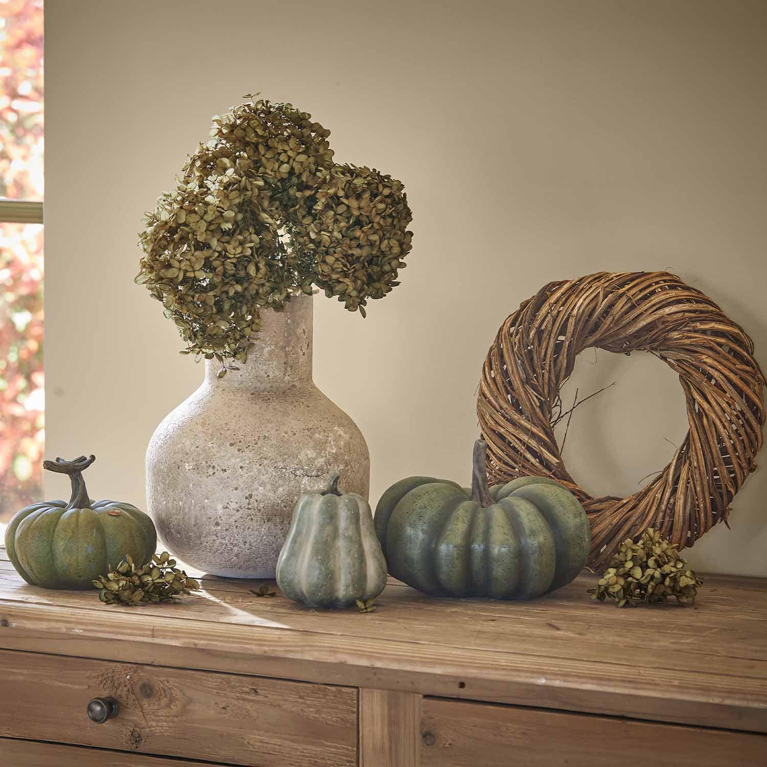 Steinvasen-Dekoration mit getrockneten Blumen und grünen Kürbissen auf Holztisch