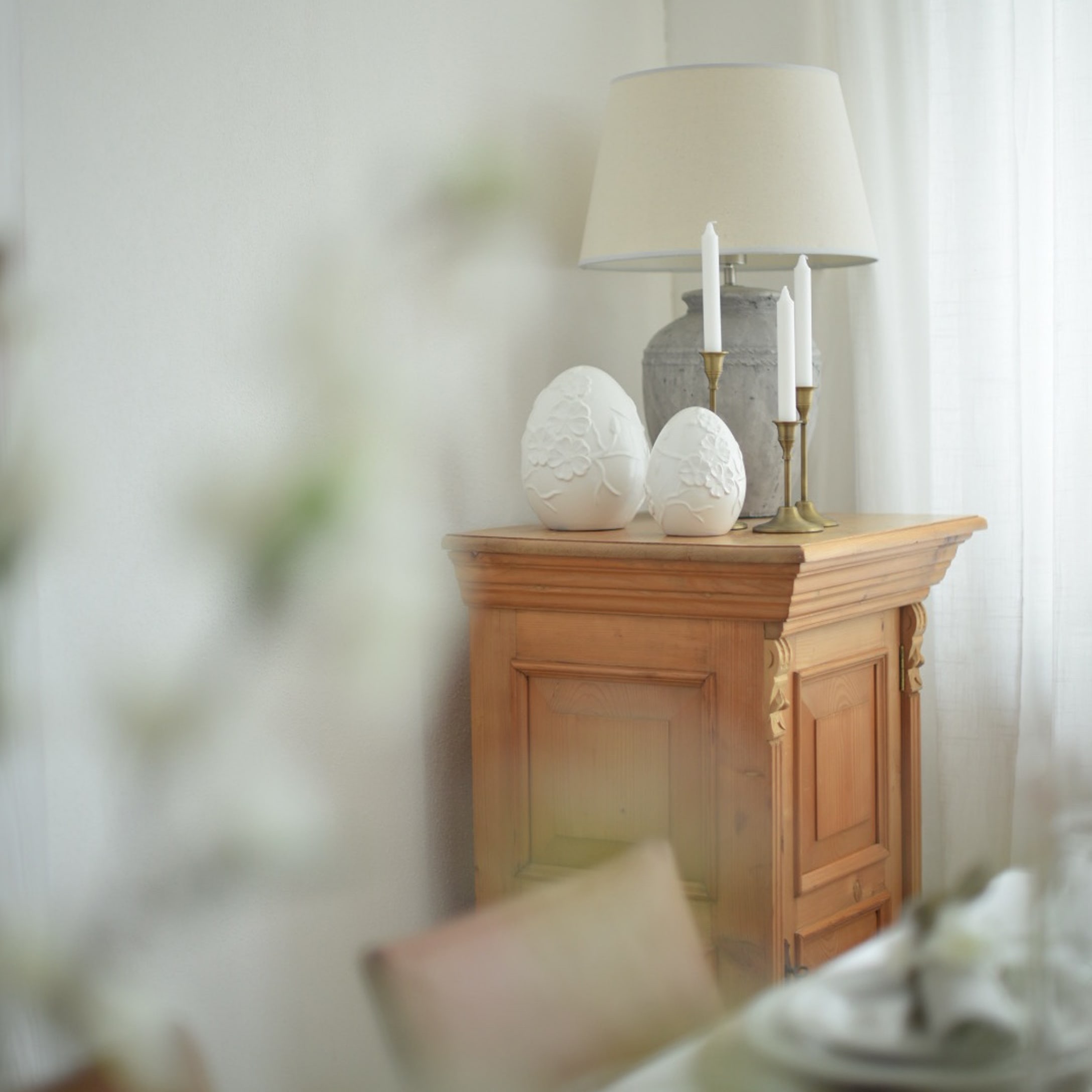 Holzschrank mit Lampe, Kerzen und weissen Keramik-Eierdekorationen in hellem Raum
