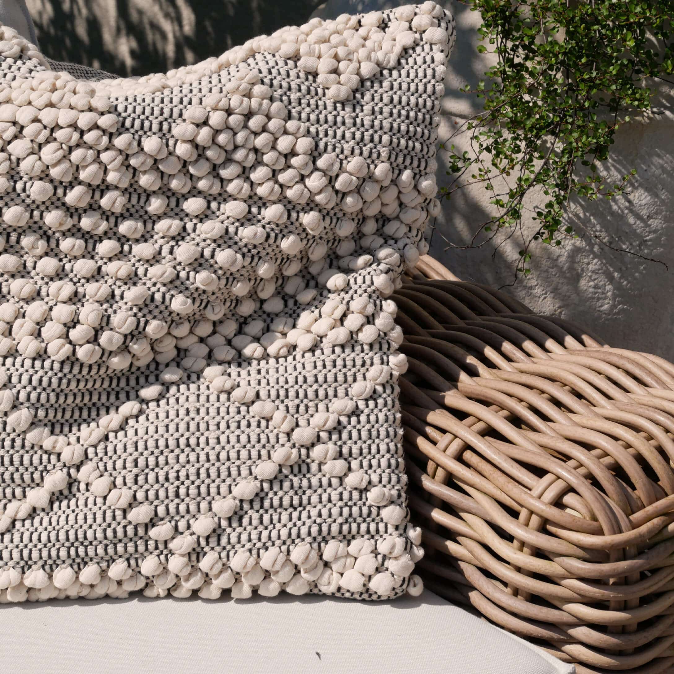 Dekoratives Baumwollkissen in Creme und Grau auf Rattansessel, Wohnaccessoire