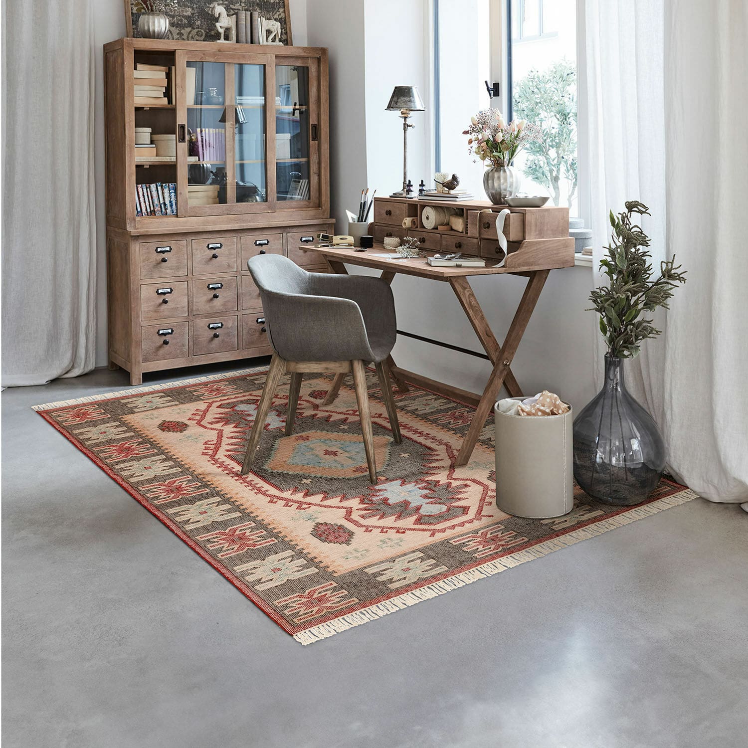 Teppich Frída Gemütliches Arbeitszimmer mit Holztisch und grauem Polsterstuhl auf buntem Musterteppich