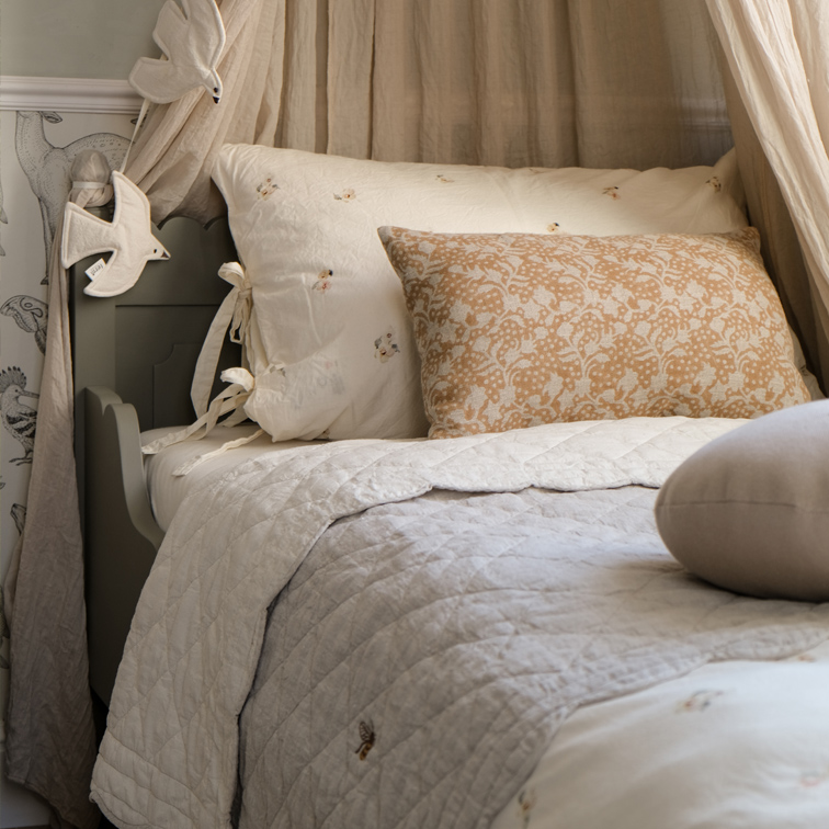 Gemütliches Bett mit beigem Kissen im Blumenmuster und hell gesteppter Baumwollbettwäsche