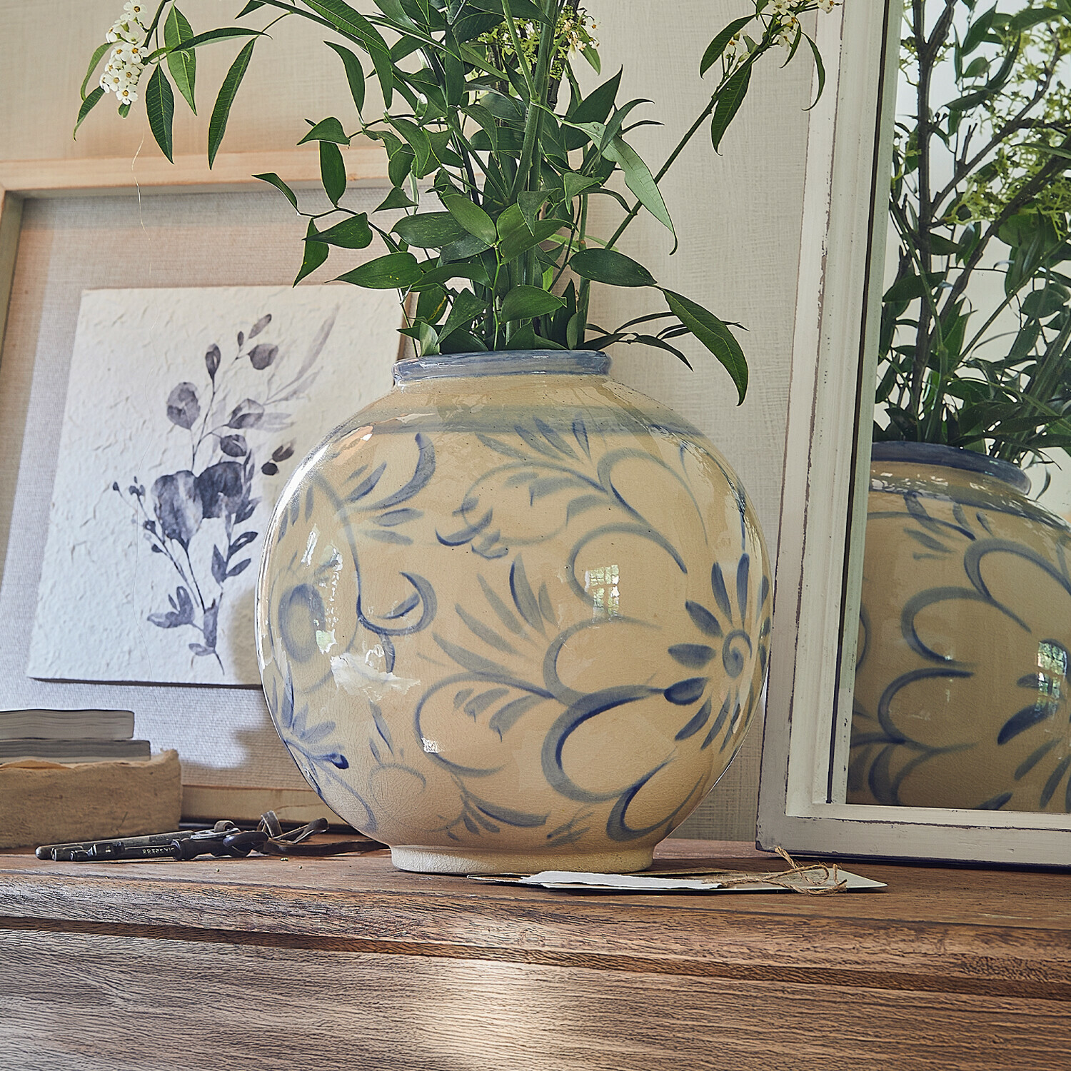 Vase Oviren Runde Keramikvase in Beige mit blauem Blumenmuster auf Holztisch mit grünen Blättern