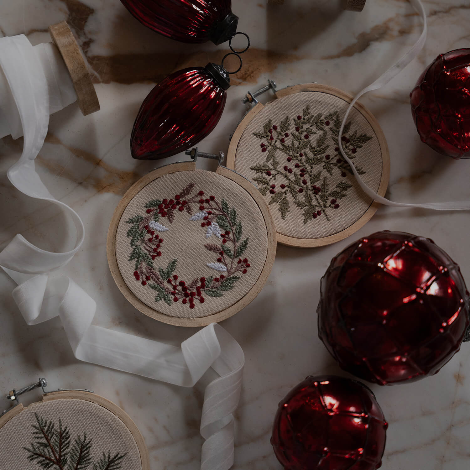 Weihnachtsschmuck mit bestickten Pflanzenmotiven auf beigem Stoff und roten Kugeln