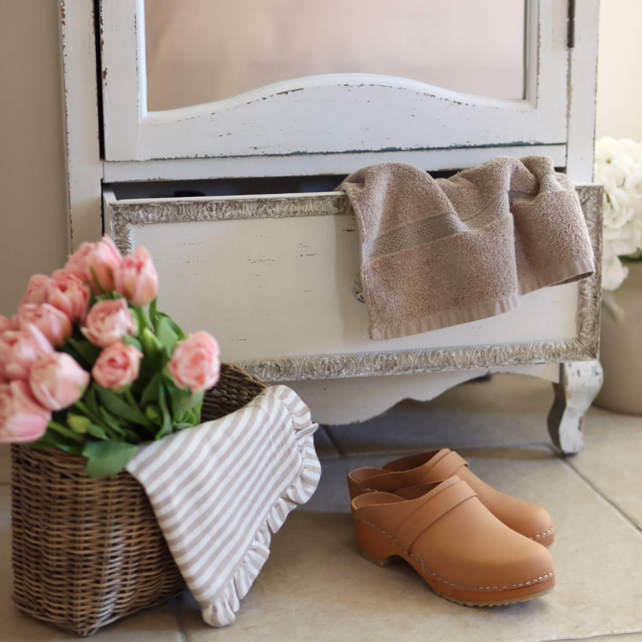 Beige Lederschuhe auf Boden neben Korb mit rosa Blumen und Handtuch in natürlichem Ambiente