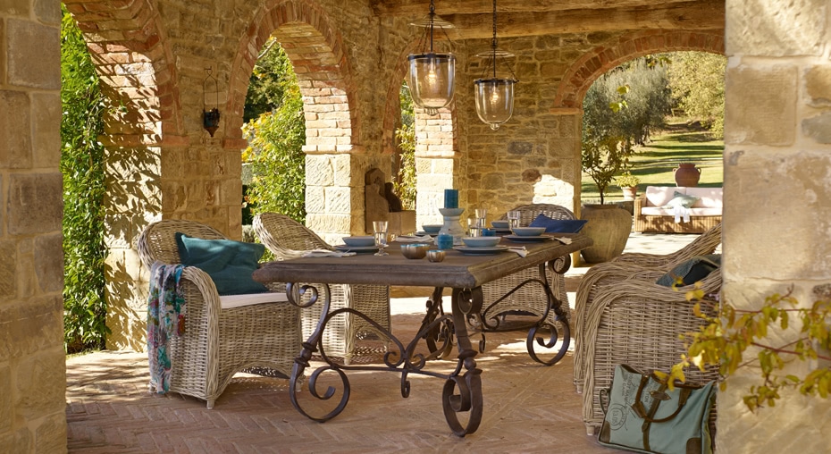 Stilvoller Tisch mit schmiedeeisernen Beinen und Rattanstühlen unter einem steinernen Bogen auf der Terrasse