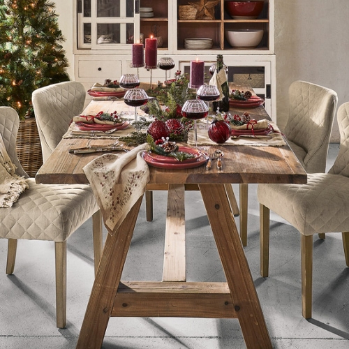 Holztisch mit beigen, gesteppten Stühlen und festlicher Weihnachtsdekoration mit roten Kerzen und Weingläsern