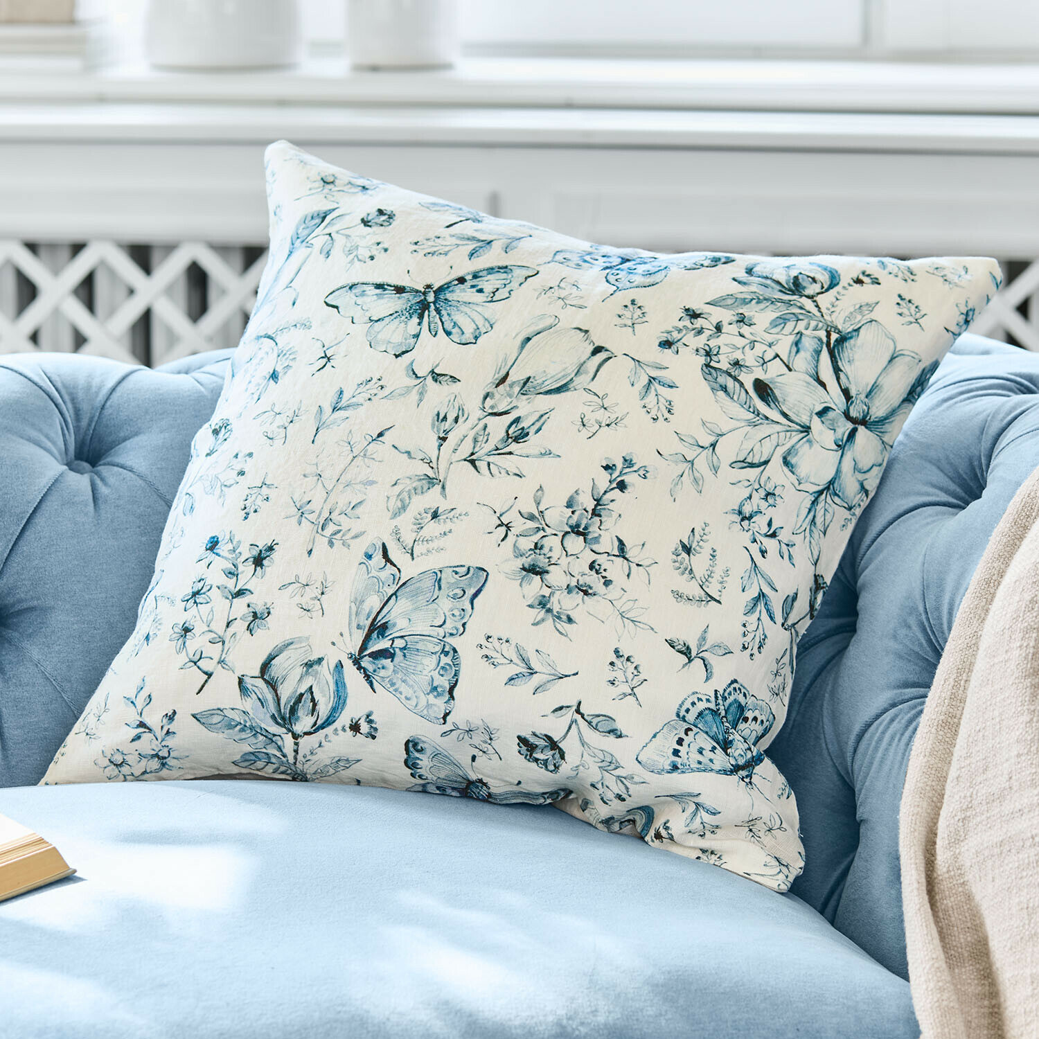 Kissenhülle Volanaïs Dekoratives Baumwollkissen in Creme mit blauem Schmetterlings- und Blumenmuster auf hellem Hintergrund