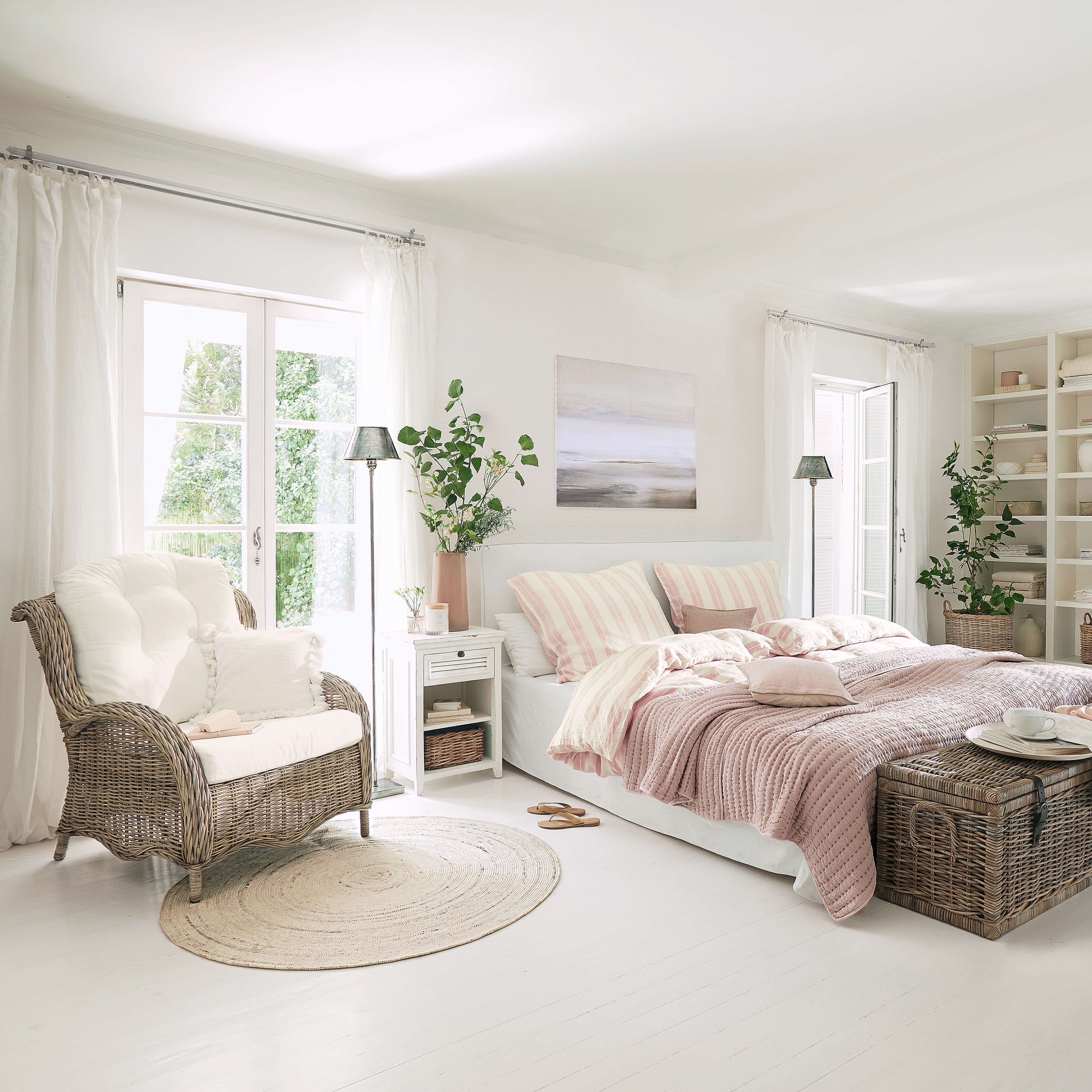 Helles Schlafzimmer mit weissem Bett, rosa Bettwäsche und Korbsessel auf hellem Boden